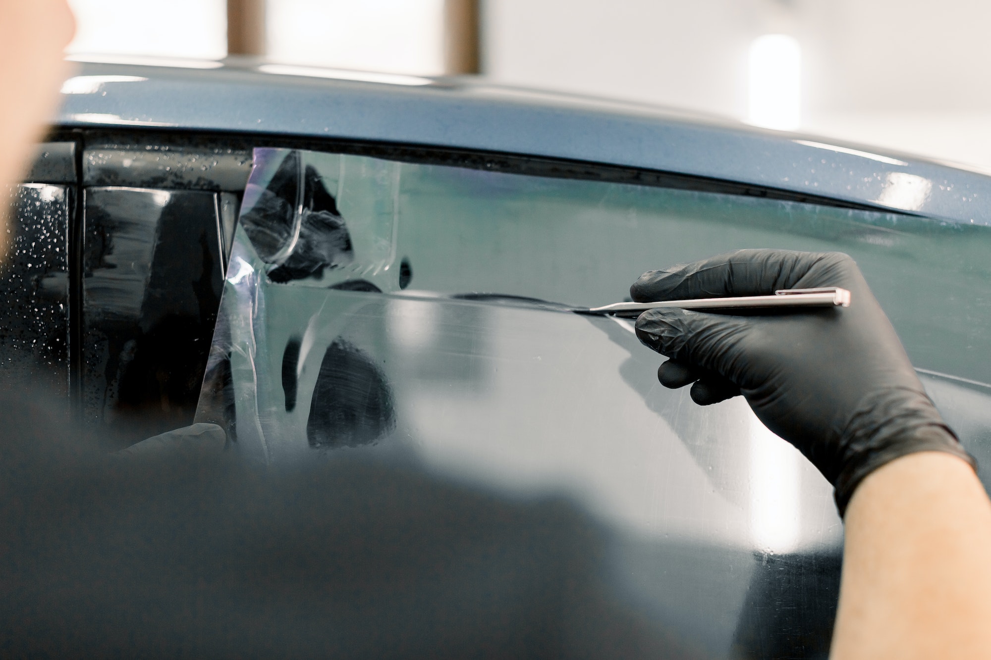 Cropped image of hands of worker in garage tinting a car window with tinted foil or film, holding